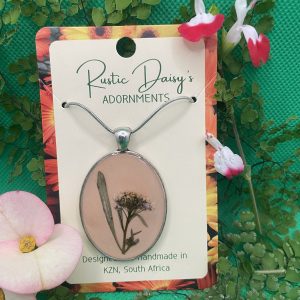 Large oval silver coloured pendant with dusty pink background and wild flower with leaf