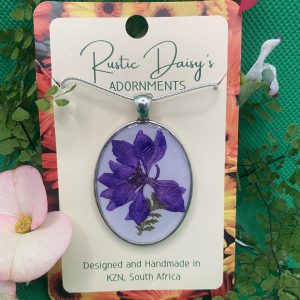 Large oval silver coloured pendant with white background and purple flower with fern leaf
